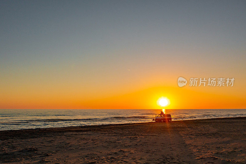 海滩上一对夫妇在露营车上享受日落的美景