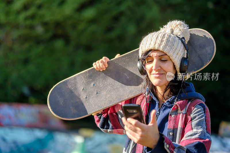 在滑板公园玩滑板的女人用智能手机发短信
