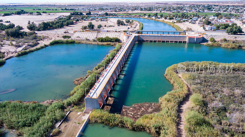 在阳光明媚的日子里，下加利福尼亚州北墨西哥，亚利桑那州尤马和阿尔戈多内斯附近国际边境墙之间的科罗拉多引水大坝河流排水的无人机视图