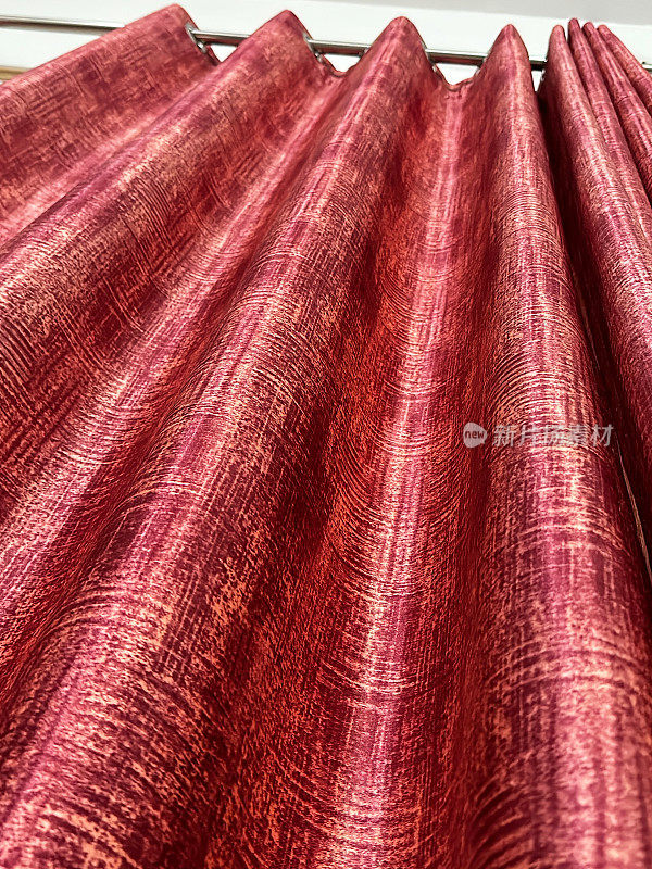 从下面看，红色、斑驳的窗帘挂在金属窗帘杆上，窗上挂着网眼窗帘