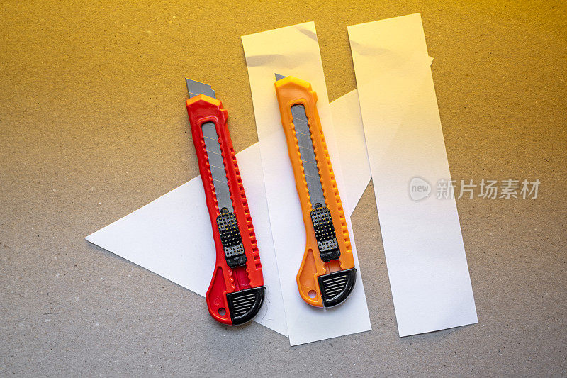 红色和橙色锋利的办公文具刀，棕色的纸板切割刀片在桌面办公桌上