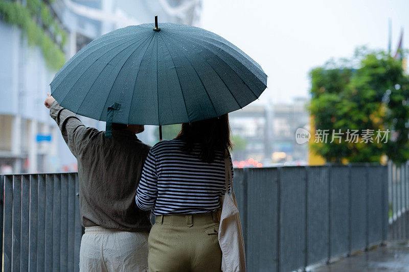 一对亚洲夫妇在下雨天打着伞一起散步