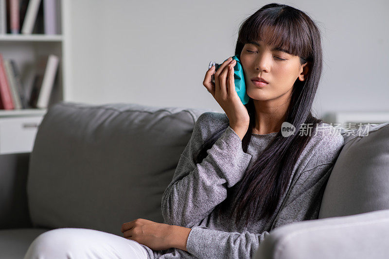 一名年轻的亚洲女子明显感到疼痛，她用冰袋敷着脸颊，这表明她可能牙痛或牙齿敏感。
