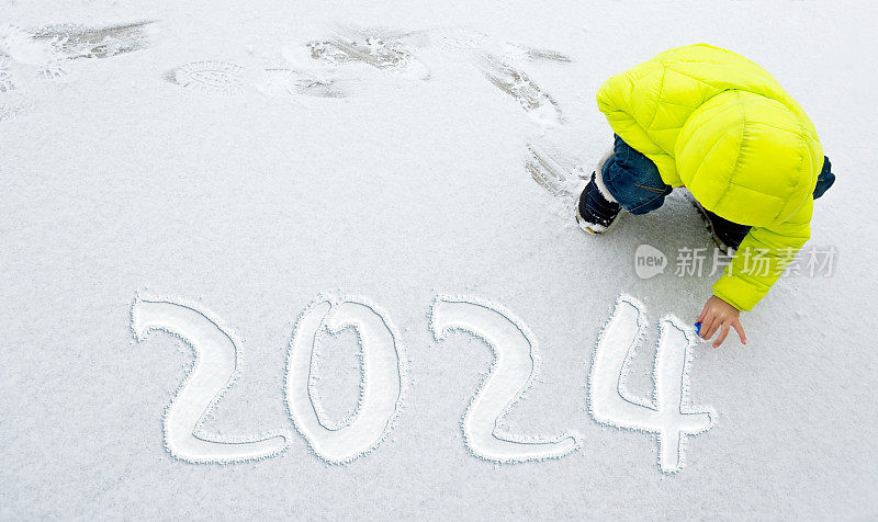 小男孩在雪地上写着新年数字2024