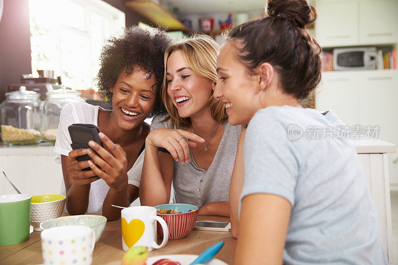 三位年轻女性朋友一边吃饭一边用智能手机