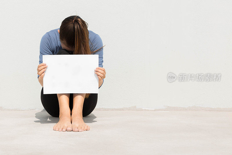 一个孤立的女人，手拿空白的白色标志，头埋在膝盖里