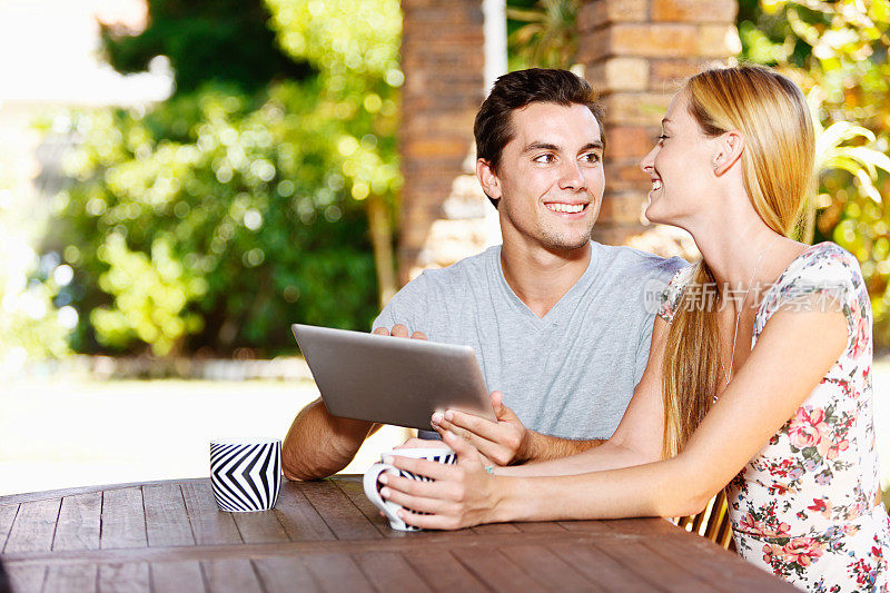 一对心满意足的夫妇坐在一起喝咖啡，分享数码平板电脑