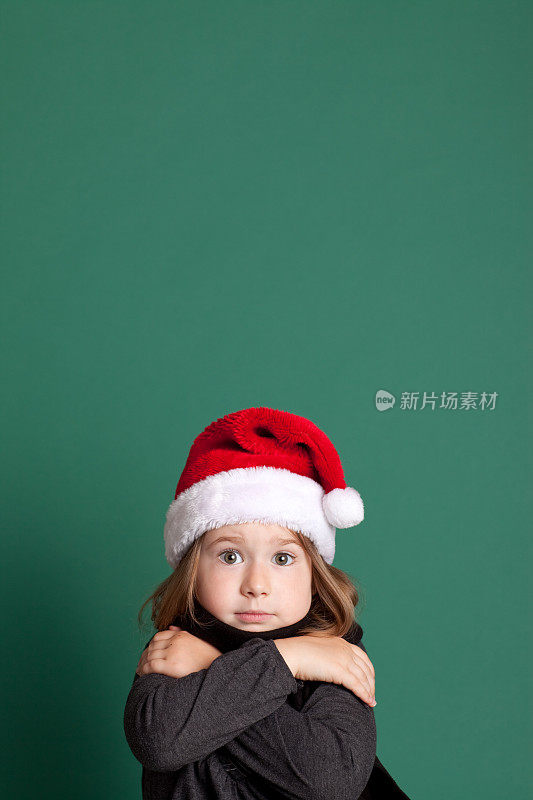 寒冷的小女孩戴着圣诞老人的帽子和围巾