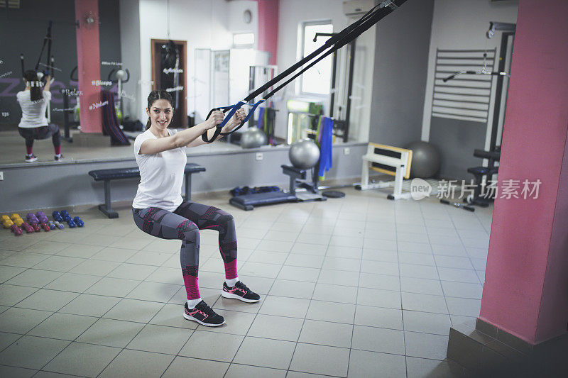 女人在健身房训练与trx健身条手臂