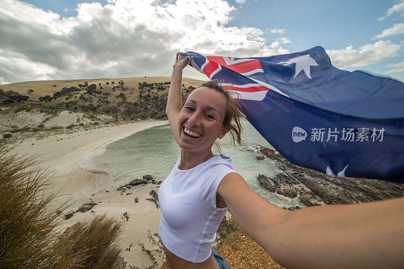 旅游妇女站在悬崖上的海滩上举着澳大利亚国旗