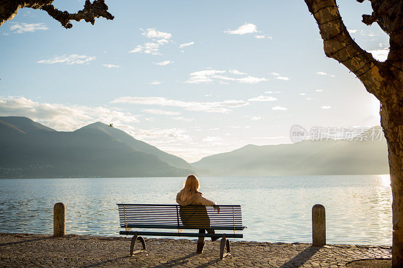 年轻女子坐在湖边的长椅上看日落