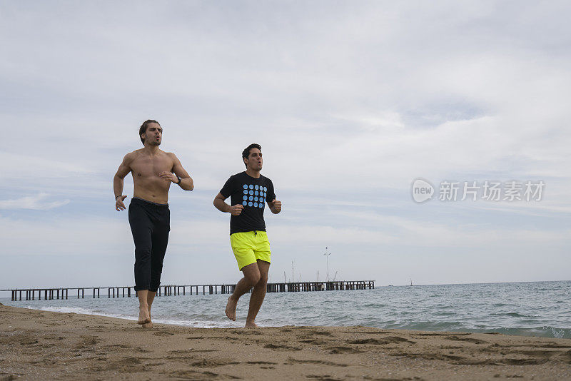 两个年轻英俊的男人在海滩上跑步