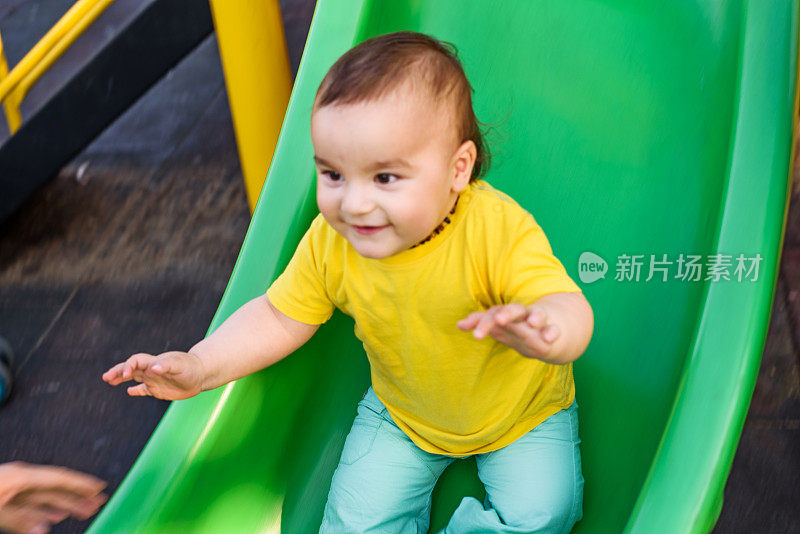 可爱的男孩愉快地在操场上玩滑梯