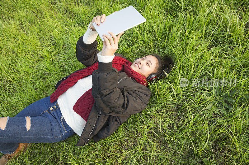 年轻女子躺在草坪上用平板电脑看电影