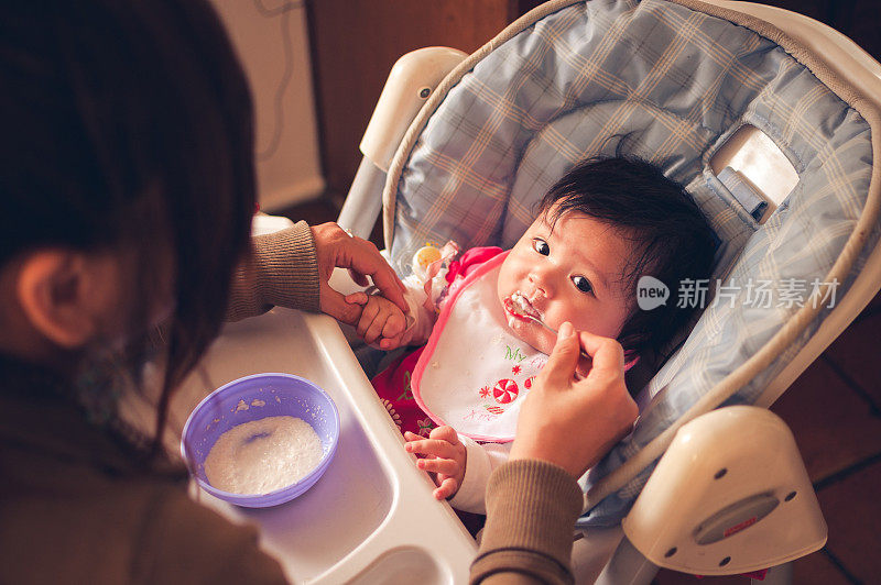 婴儿欧亚女孩坐在高椅子上被喂食