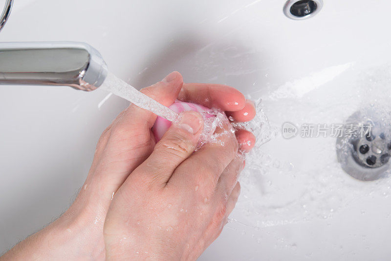 在有粉红色肥皂的水流下，双手被打上了肥皂
