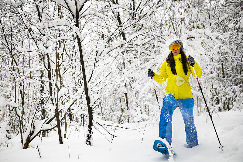 勇敢的徒步旅行者用她的雪鞋和登山杖在田园诗般的冰冻森林的厚厚的积雪中艰难跋涉