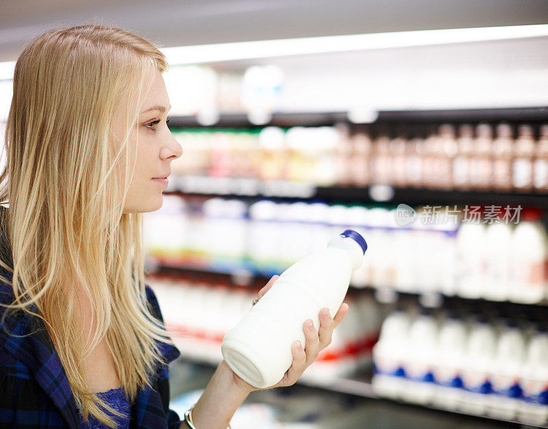 美丽的金发女人微笑着从超市冰箱里拿牛奶