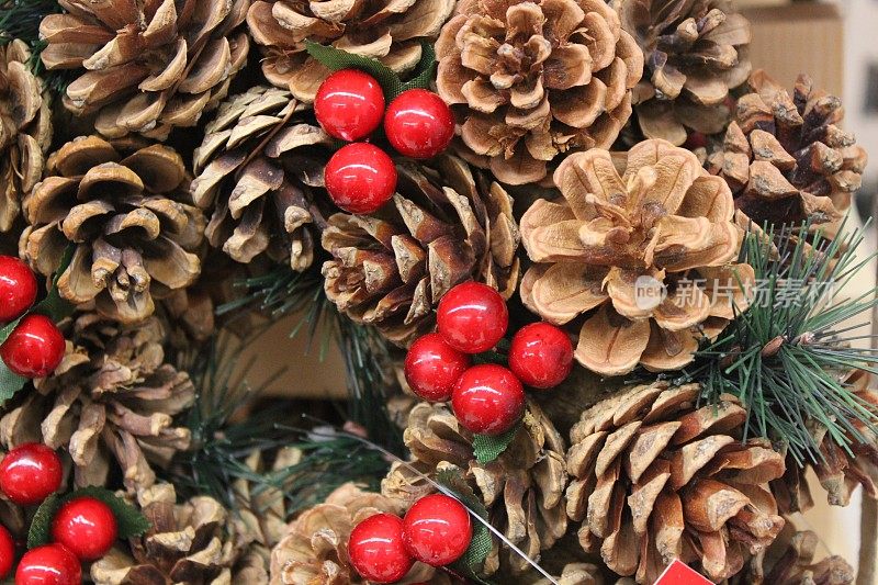 圣诞花环的特写图片，人造云杉针，干燥的松果和塑料红冬青浆果，季节性的装饰出售