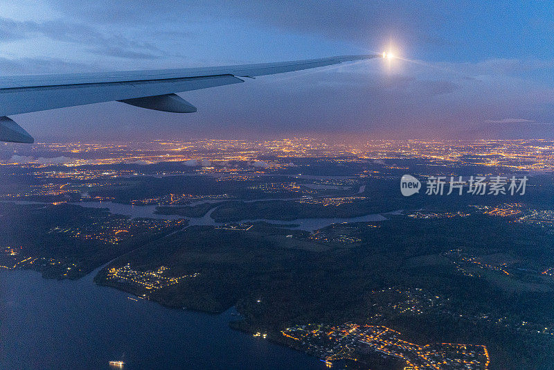 这架飞机的机翼在国际飞行中迎着天空和云层，鸟瞰着灯火通明的城市夜景。