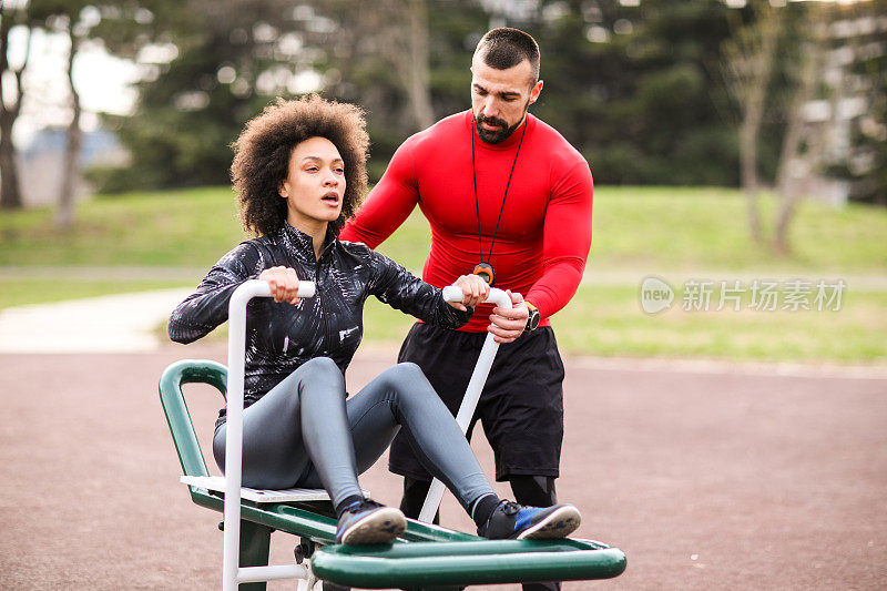 肌肉私人教练指导一位女运动员在城市公园的划船机上锻炼