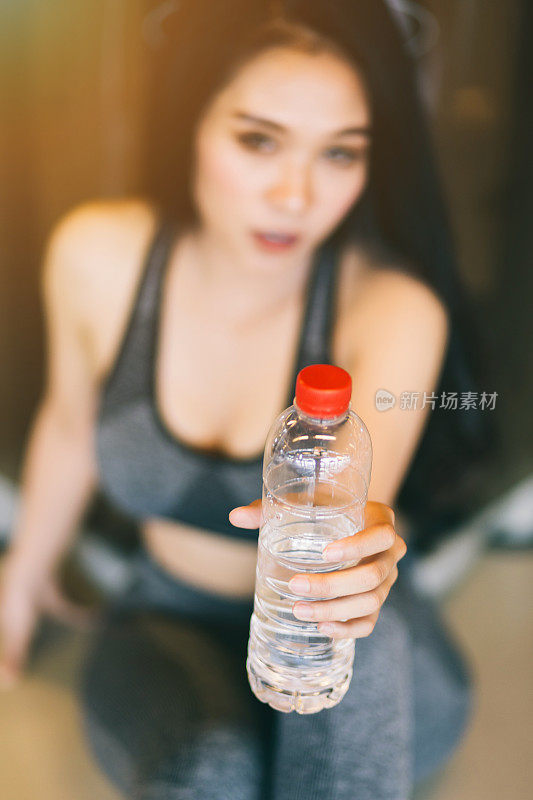 特写亚洲妇女进行锻炼训练，如何在体育健身室内和健身健身俱乐部与体育锻炼设备健身房背景的一瓶水。