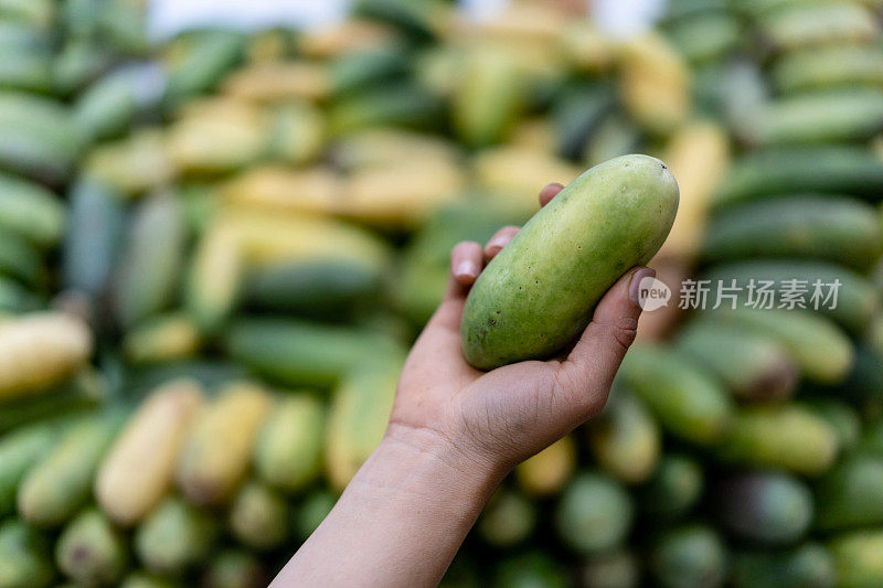 近距离观察，一个农贸市场上一个面目全的女售货员拿着一个香蕉百香果