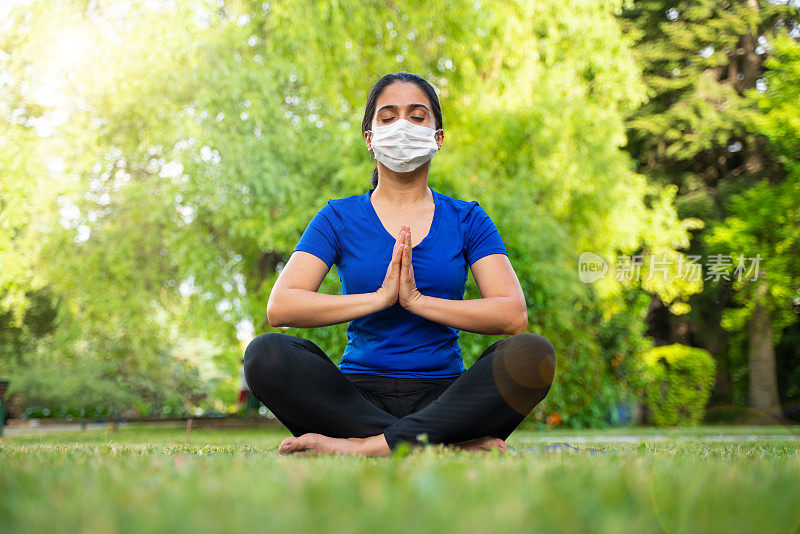 在流感大流行期间，为了保持健康，妇女戴着防护面罩在户外做瑜伽