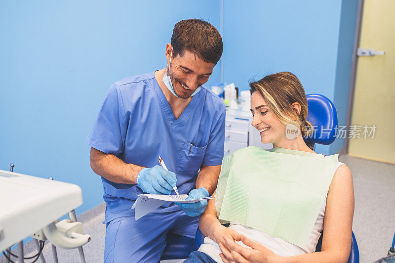 牙科医生在牙科诊所写结论和诊断。口腔医学与健康理念。年轻英俊的男医生戴着一次性医用口罩和手套与快乐的女人微笑。