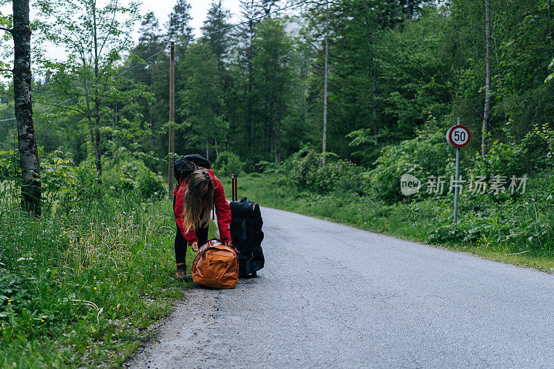 年轻女子背包客在雨中等待在路边与行李