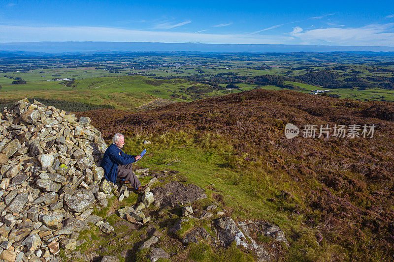 高角度的高级男子看地图，而坐在旁边的一个石碑上的苏格兰山顶