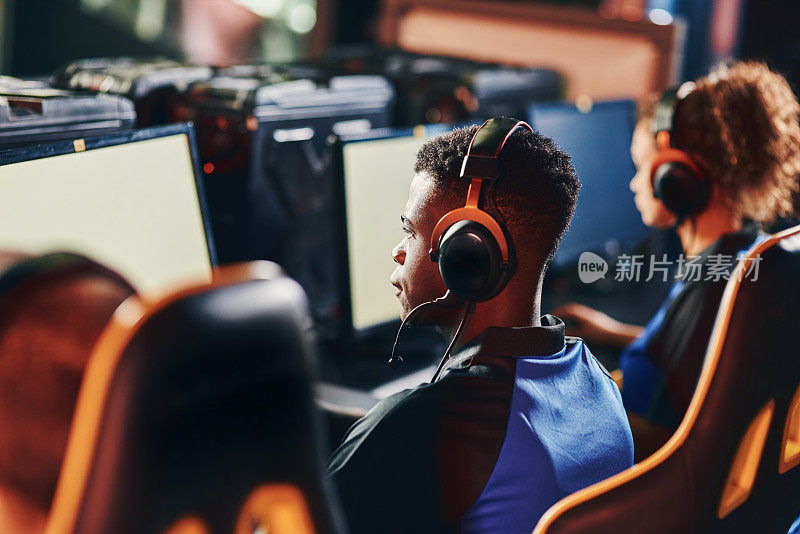 专注的年轻非洲人的后视图，专业电子竞技玩家戴着耳机玩在线视频游戏，参加电子竞技比赛