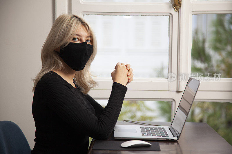 年轻女子戴着面具在家使用笔记本电脑工作