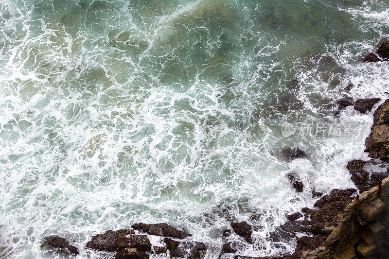 Arial视图的波浪打破到一个岩石的海岸线，背景与复制空间