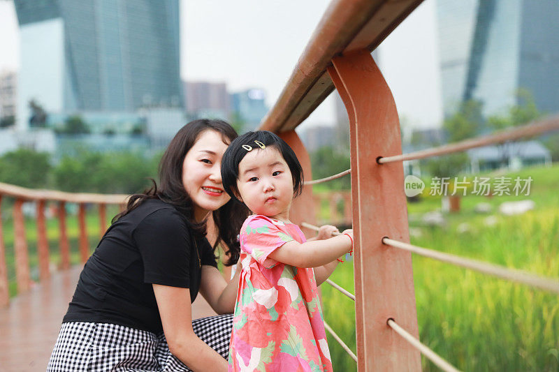一个中国女孩看着镜头，她的妈妈在后面微笑