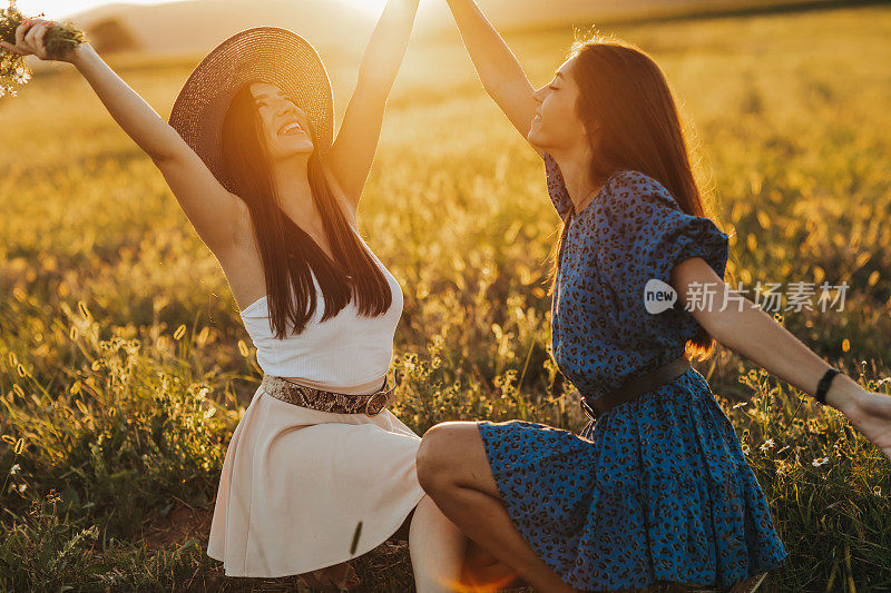 两个年轻的女性朋友在盛开的草地上享受阳光灿烂的夏日日落