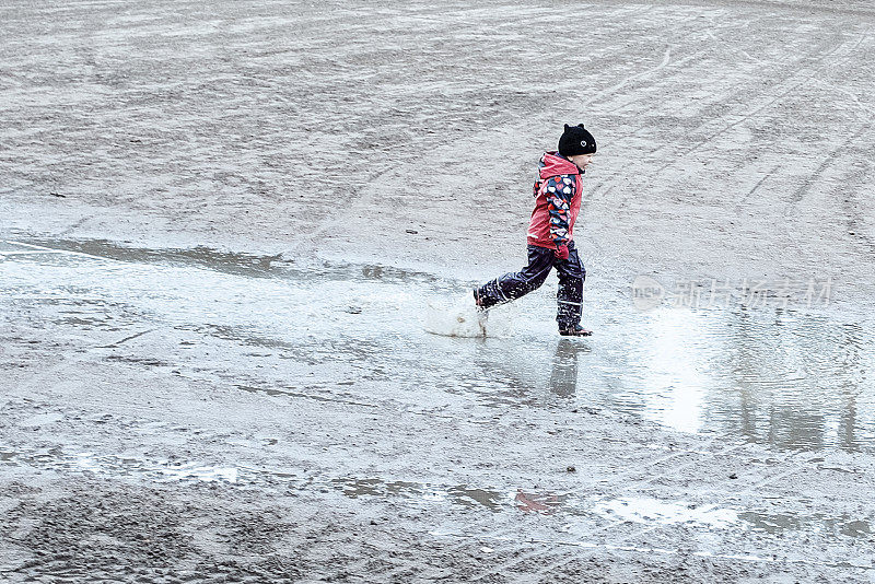 一个穿着防水儿童服的孩子玩得很开心，跑过水坑。Deaochka是一个5岁的白种人，她非常喜欢在水坑里跑步。