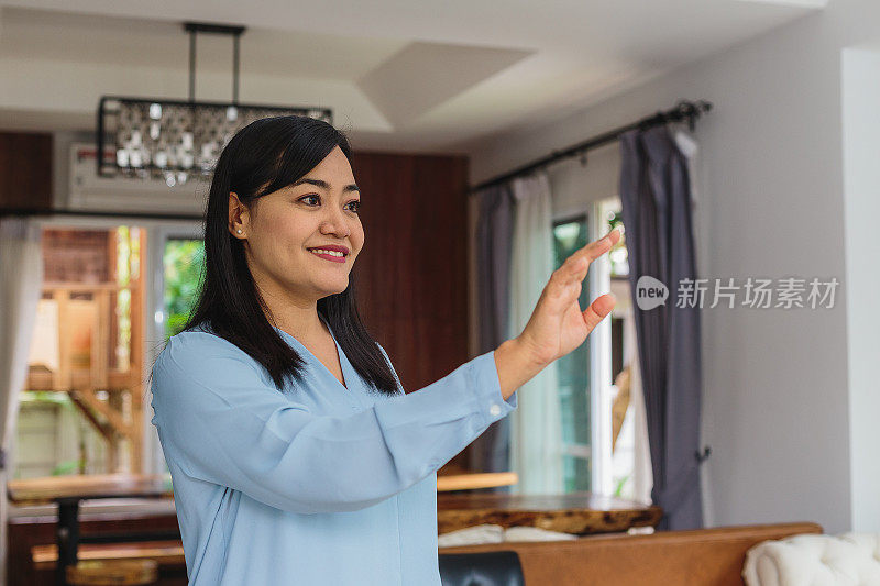 亚洲成熟女性在家庭客厅使用智能表面或UX界面(空白表面墙)，智能未来家居和物联网概念