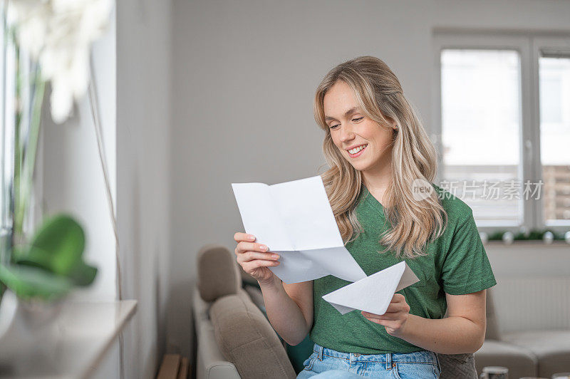 年轻女子微笑着在家里读一封信