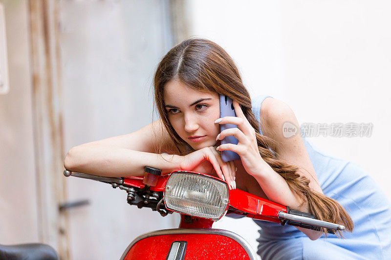 年轻女子坐在红色踏板车上打电话