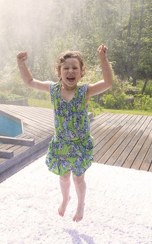 6岁的小女孩高兴极了，在水花中跳来跳去。夏天的炎热和在乡村小屋的放松。
