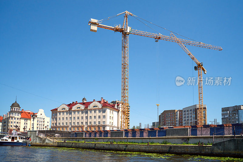 建筑工地与起重机和多层建筑在河边，蓝天为背景