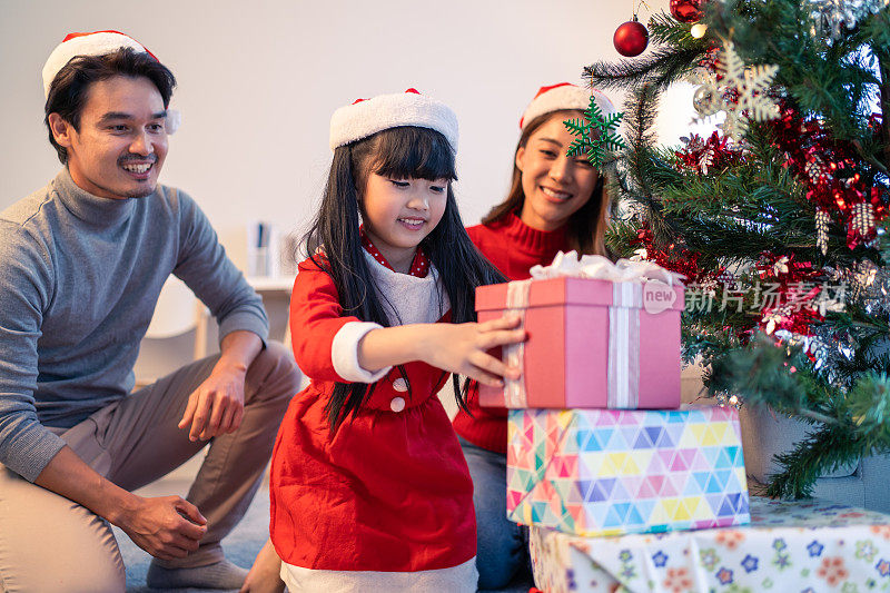 亚洲可爱的家庭成员用幸福装饰圣诞树。年幼的女儿心情愉快，兴奋地和父母一起在家里庆祝节日圣诞节感恩节聚会。
