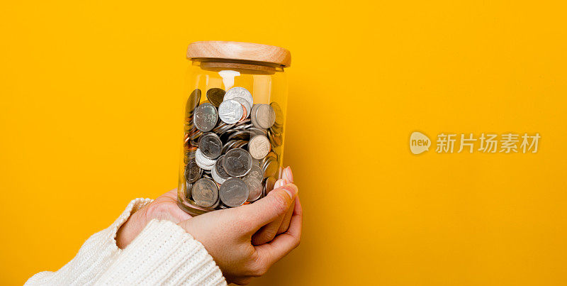 省钱。年轻女子的手拿着一枚硬币放在玻璃杯里。财务会计的省钱理念。