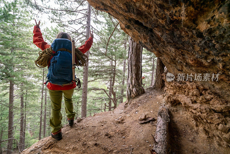 女登山者在落基山的山洞里，一边看森林、峡谷的美景，一边做着“和平手势”