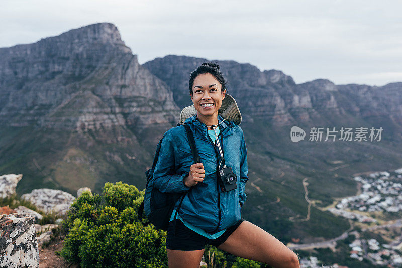 一名年轻女性徒步旅行者的肖像，穿着模拟相机和背包站在山顶上，看向别处