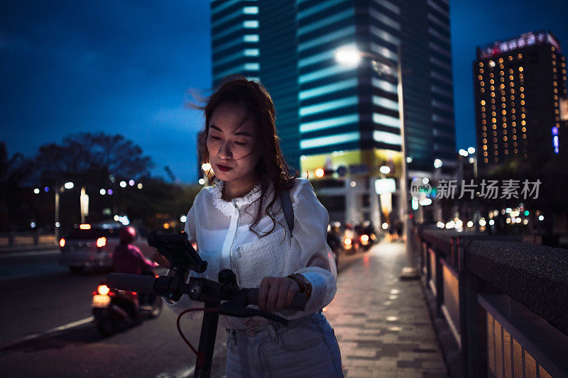 亚洲中国女人在城市里骑电动车，用智能手机