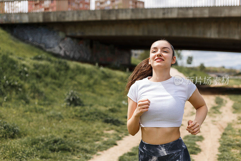 女孩在中午的阳光下在河边跑步。