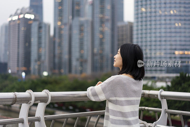 在市中心的一座桥上，一位亚洲妇女望着远方