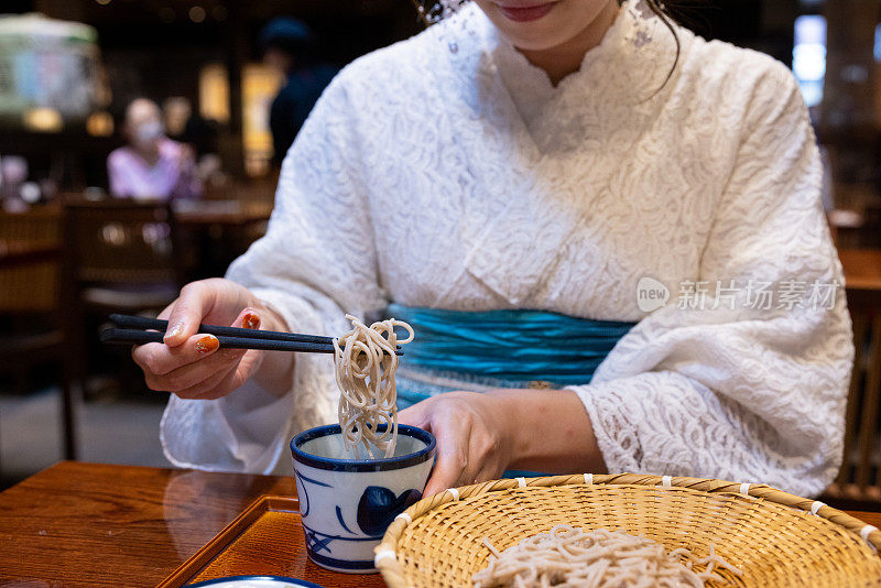 特写和服妇女的手吃荞麦为午餐在日本餐厅